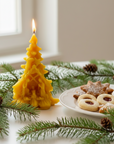 Yellow Christmas tree candle with a plate of cookies and pine branches on a light background.pine tree beeswax candle with nativity scene catholic christmas gifts. 100% catholic beeswax candle