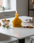 Christmas beeswax candle in the shape of a house on a table with christmas food