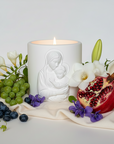 Candle with a religious figure surrounded by fruits and flowers on a white surface