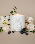 White candle with a religious design surrounded by flowers and berries on a beige background