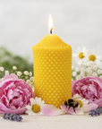 Yellow beehive-patterned beeswax candle with pink flowers and a bee on a light background