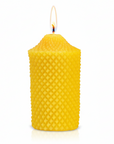 Yellow pure beeswax textured candle on a white background with a flame