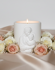 Candle with a figurine of a mother Mary and child Jesus surrounded by flowers on a satin surface