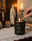 Person lighting a candle labeled 'Live Your Faith' with religious statues and bible in the background.