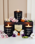 Three lit candles in black containers with visible labels on an elegant background with flowers