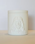White ceramic jar with embossed face design on a beige surface