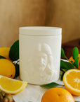 White jar with the face of Jesus surrounded by fruits and leaves on a table.