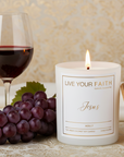 Catholic scented prayer Candle labeled "Jesus" with a glass of red wine and grapes on a patterned surface scented in merlot