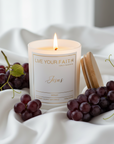 Catholic Candle labeled Jesus with grapes on a white fabric background, merlot scent.