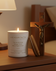 Candle labeled 'Live Your Faith' next to a crucifix on a wooden surface with a blurred background