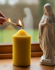 Person lighting a beeswax candle next to a statue of a Virgin Mary indoors.