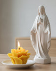 beeswax prayer candle on the shape of a rose in a white background next to a statue of Virgin Mary