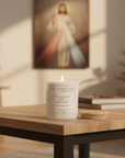 Candle with 'Live Your Faith' text on a wooden table, blurred religious painting in the background