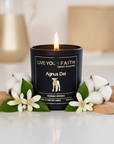Candle with 'Live Your Faith' label surrounded by flowers and leaves on a white surface