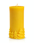 A yellow beeswax candle with an intricate pine tree detail along the bottom edge.