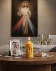Living room with a table featuring a lit candle, photo frame, and wine glasses, with a religious painting in the background.