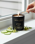 Candle in a black container with 'Live Your Faith' branding on a white window mill being lit up by female hand.