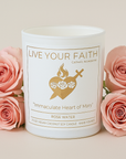 Candle with 'Live Your Faith' label surrounded by pink roses on a light background Immaculate Heart of Mary candle