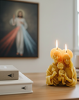 Beeswax candles shaped like the Holy family on a table with a religious painting in the background.