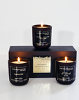 Three lit candles in black containers with visible labels on a white background