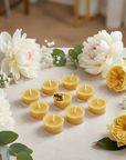 Set of small yellow candles surrounded by white and yellow flowers on a light surface.