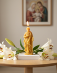 candle shaped like Saint Joseph with white lilies on a wooden table, framed artwork in the background.