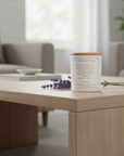 St. Theresa of Avila Candle on a wooden table with a blurred living room background and lavender leaves