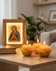 three lit beeswax rose candles with a Virgin Mary Icon and a bible on a table in a cozy living room.