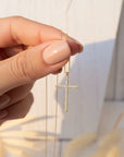 Hand holding a gold cross necklace with a blurred background