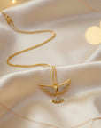 Gold necklace with a dove shaped pendant on a soft fabric background
