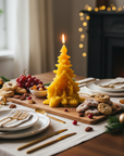 Decorative candle shaped like a Christmas tree on a table with food and festive decor. pine tree beeswax candle with nativity scene catholic christmas gifts