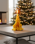 Tree-shaped candle on a table with a Christmas tree and fireplace in the background, pine tree beeswax candle with nativity scene catholic christmas gifts. 100% beeswax candle.