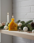 Decorative setup with beeswax candles and greenery on a shelf against a white brick wall.