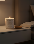 Candle with Bible verse John 1:14 in a nightstand next to an open bible in a dimly lit room.