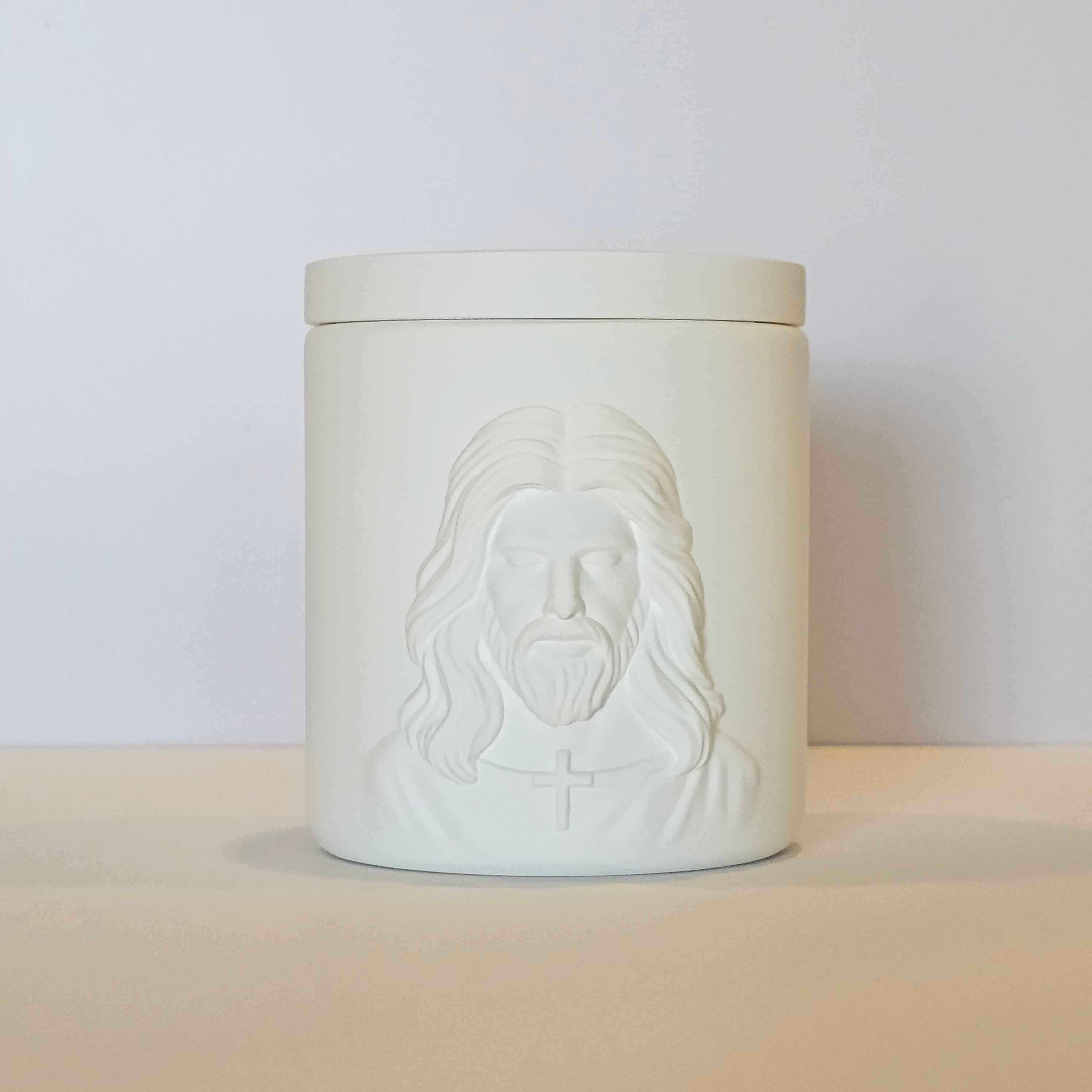 White ceramic jar with embossed face design on a beige surface