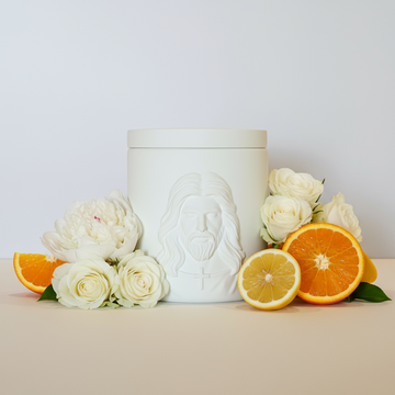 White ceramic jar with embossed face design on a beige surface with flowers and citrus fruits