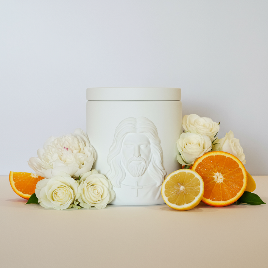 White ceramic jar with embossed face design on a beige surface with flowers and citrus fruits