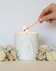 Hand lighting a candle with a match, surrounded by flowers on a light background