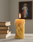 Candle with a religious design  of the holy family next to books on a table, with a blurred background