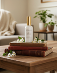 room spray bottle on a stack of books with flowers on a wooden table in a living room, with the words "Jesus, I trust in you"