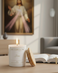 Candle with Jesus text on a table in a room with a painting of the divine Mercy figure in the background.