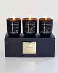 Three black candles with labels on a black box with a gold tag, against a white background.