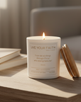 Candle with 'Live Your Faith' text on a wooden surface with books in the background