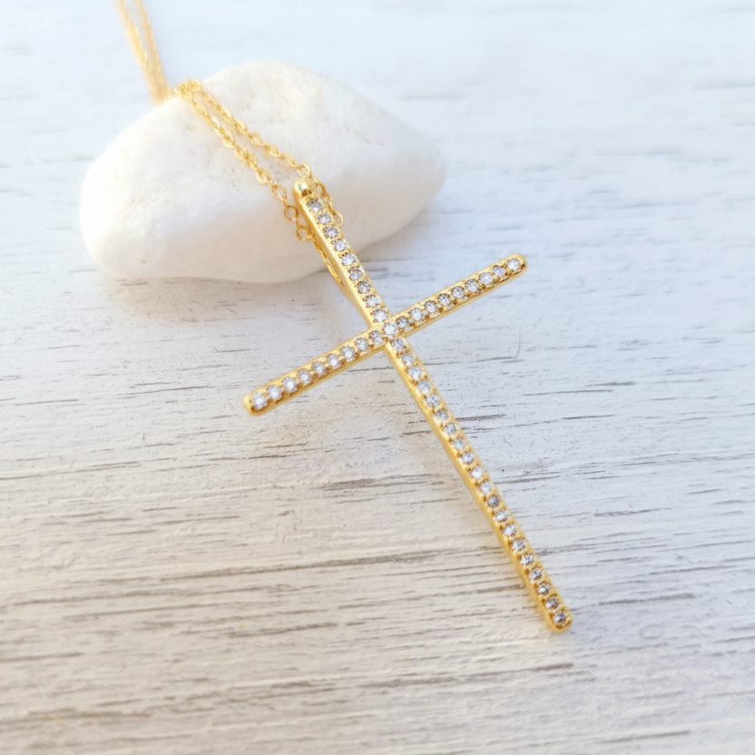 Gold cross necklace with clear stones on a light wooden surface
