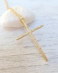 Gold cross necklace with clear stones on a light wooden surface