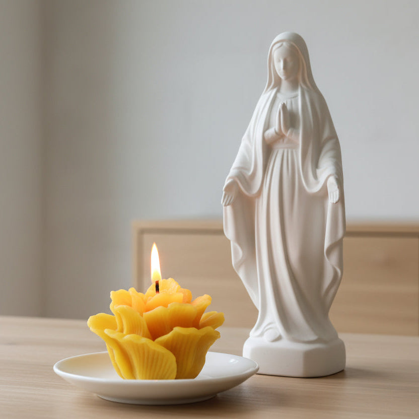 beeswax prayer candle on the shape of a rose in a white background next to a statue of Virgin Mary