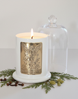 White candle with a gold emblem and clear glass lid on a white background