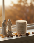 Candle with Bible verse John 1:14 surrounded by frankincense and myrrh on a blurred background on a windowsill with nativity figurines and candles.