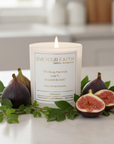 Candle with 'Live Your Faith' text surrounded by figs and leaves on a table.