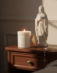 Candle with 'Live Your Faith' packaging, statue of a religious figure, and rosary on a wooden surface.